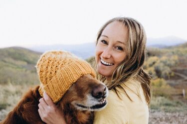 A woman holding her dog wearing a hat.