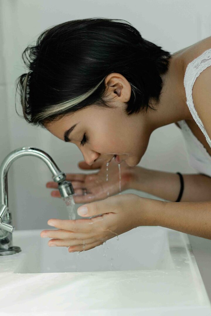 A woman is washing her face in the sink.