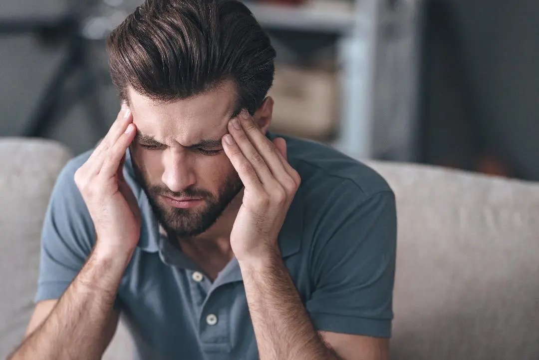 A man sitting on the couch with his hands in his head.