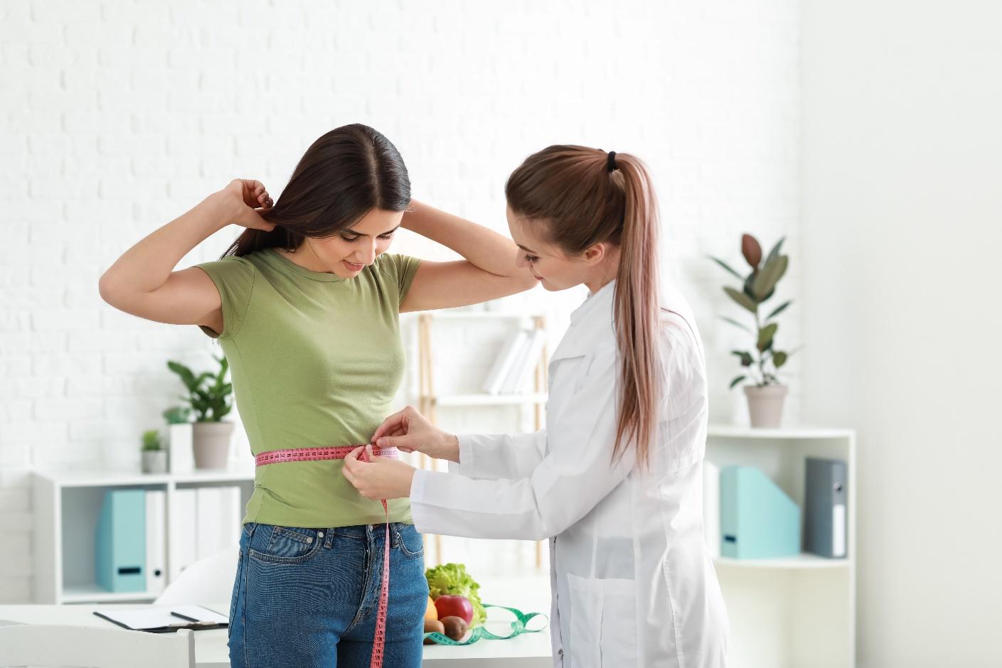A woman is measuring her waist with a doctor.