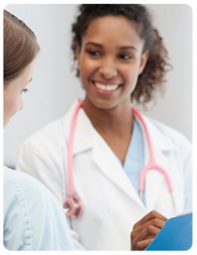 A woman in white coat holding a book and smiling.