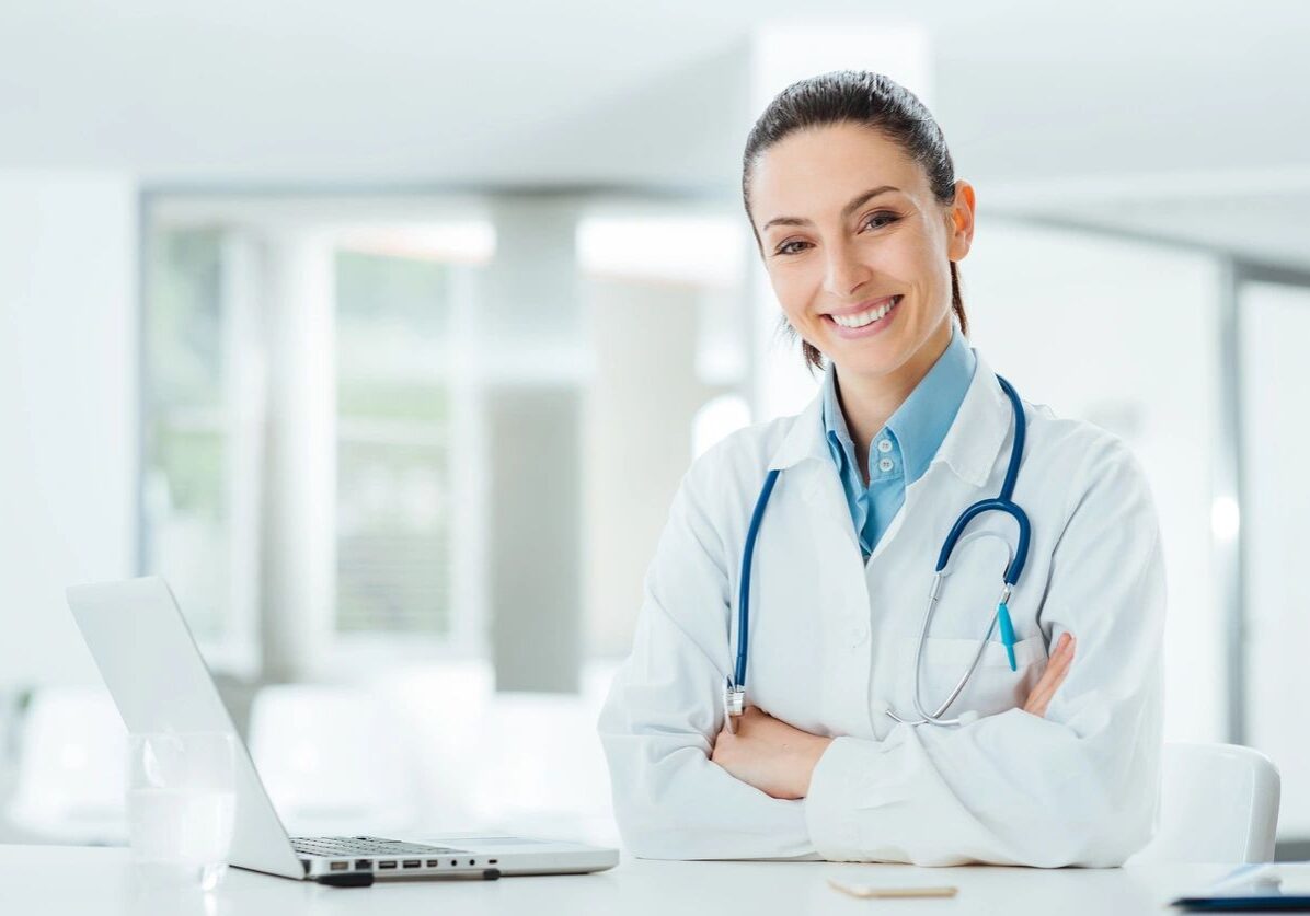 Smiling doctor with stethoscope at desk.